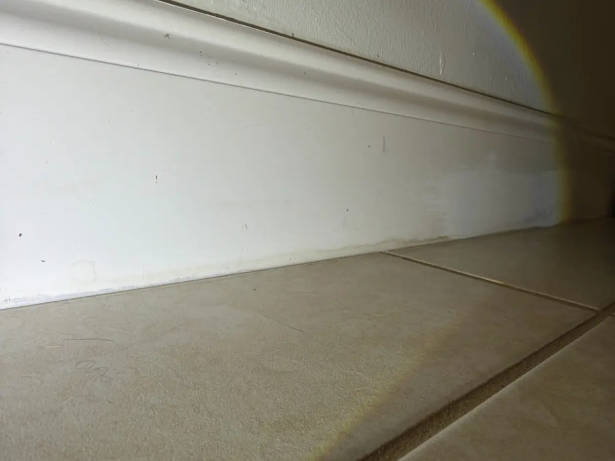 Water staining along a baseboard above a tile floor, a sign of past moisture damage that calls for mold air sampling